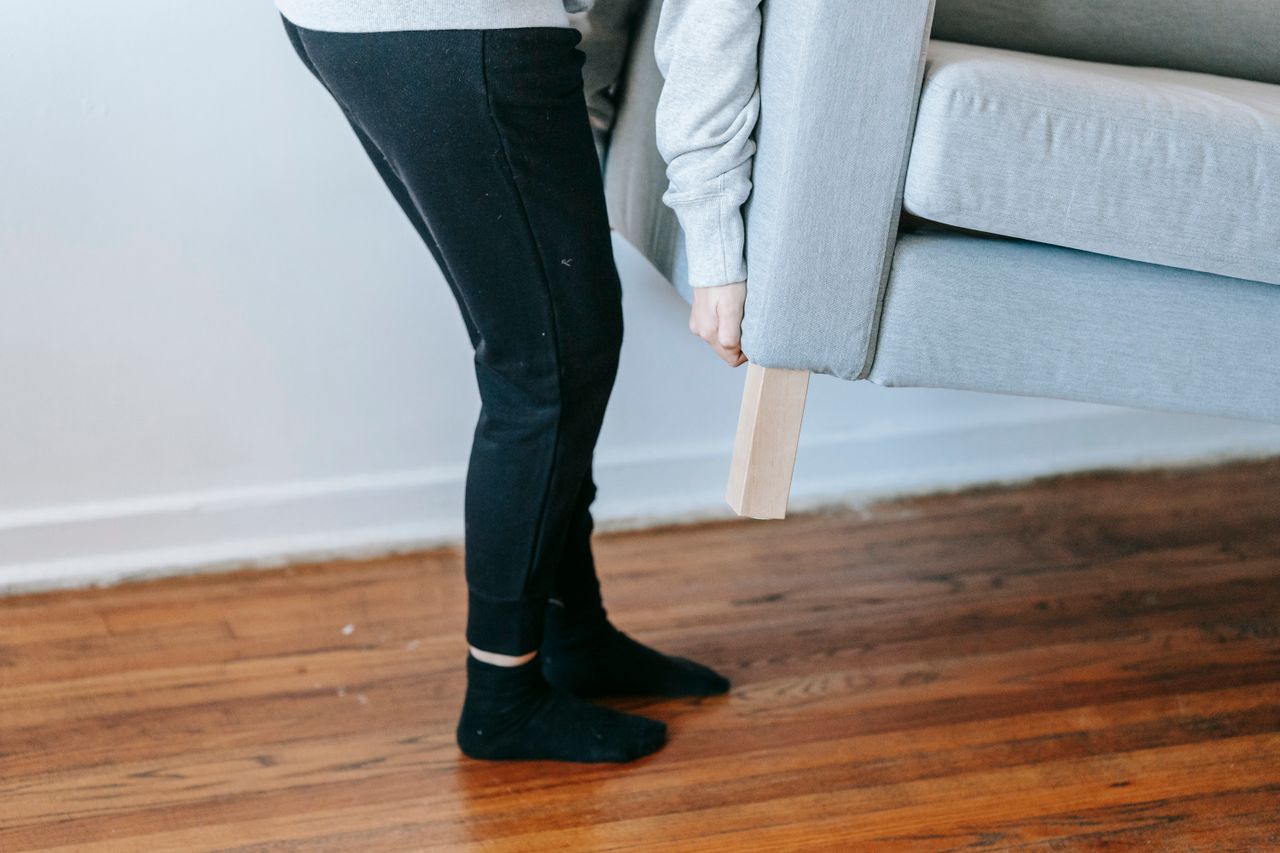 team-01 A person lifting a couch in a minimalist living room with wooden floors.